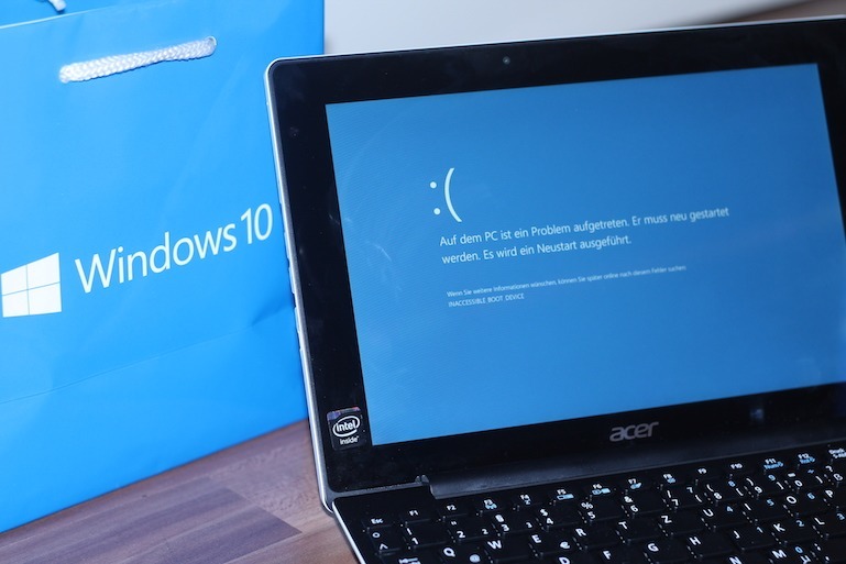 Titelbild des Artikels. Es zeigt einen Windows 10 Notebook, der gerade einen Bluescreen darstellt. Dahinter befindet sich eine Windows 10 Tüte für die Optik.